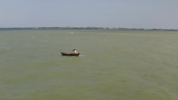 タンザニアのダルエスサラームの海岸近くの晴れた日に風と波に対して木製のカヌーボートを漕ぐ男 — ストック動画