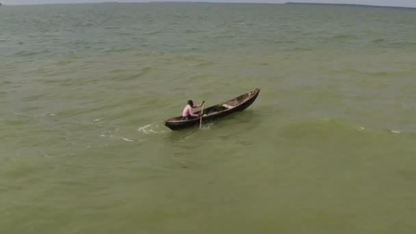 タンザニアのダルエスサラームの海岸近くの晴れた日に波と風に対して木製のカヌーボートを漕ぐ男 — ストック動画