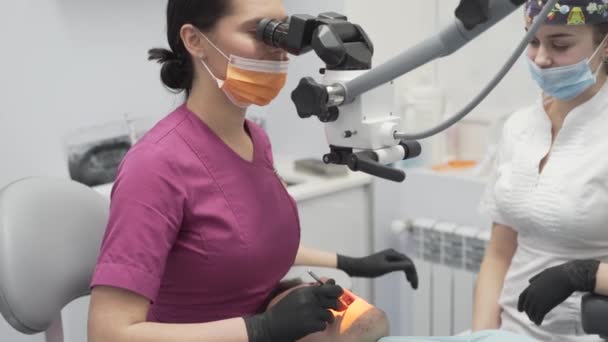 診療所で現代の歯科顕微鏡を使った患者の口内検査を行う女性歯科医 女性医療看護アシスタントプレゼント — ストック動画