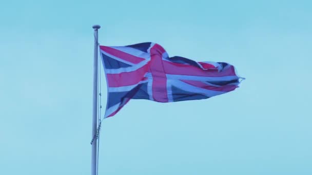 ユニオンジャックフラッグが風に揺れる ライトブルーの空に立ち向かうイギリスの国旗 — ストック動画