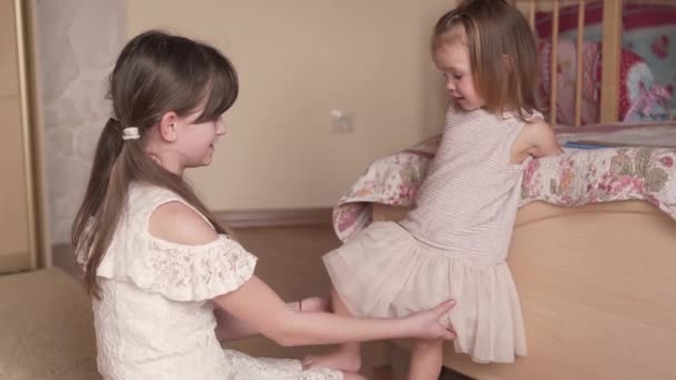 白いドレスとピグテールの姉は寝室で彼女の妹と遊んで彼女のドレスは完璧に見えます 赤ちゃんの女の子はカメラを見て — ストック動画