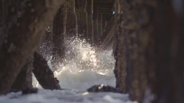 桟橋の下で波がクラッシュし 太陽の光が差し込む古い木製の杭 — ストック動画