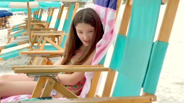 海滩上一个坐在海滩椅子上的女孩放松下来 在镜头前挥挥手 — 图库视频影像