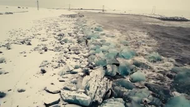 映画的なドローンの動きは 雪の多い状況で無人機によって撮影されたアイスランドの黒い砂のビーチを示しています 異なる角度は 曇った日没の光の中で海の波に見舞われたダイヤモンドビーチを示しています — ストック動画