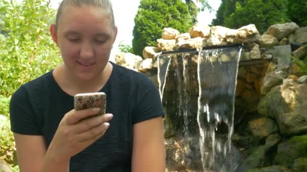 Schattige Jonge Vrouw Lacht Een Sms Haar Telefoon Terwijl Zomerschaduw — Stockvideo