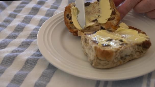 皿の上のホットクロスパンにスローモーションパンはイースターの間にキッチンナイフでバター付けされています — ストック動画