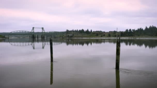 ドローン2つの木製の極 日の出ピンクの色の間にコキル川の上に低く飛んでいます 背景にはオレゴン州バンドン近郊のブラルズ橋がある — ストック動画