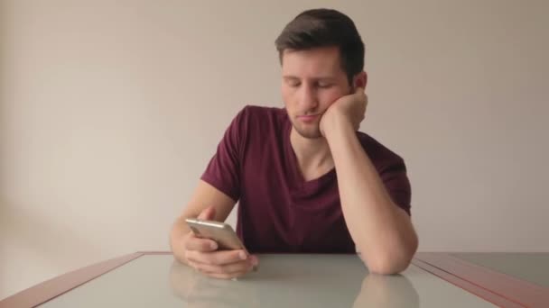 Junger Mann Schaut Gelangweilt Auf Handy Während Tisch Minimalistischer Einrichtung — Stockvideo