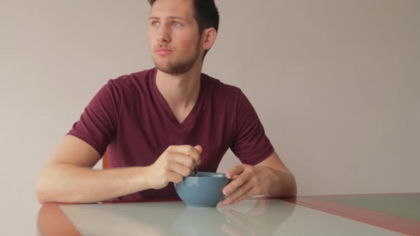 Junger Mann Sitzt Tisch Und Isst Müsli Mit Neutralem Gesichtsausdruck — Stockvideo