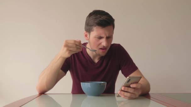 Junger Mann Der Müsli Isst Und Telefon Angewidert Und Überrascht — Stockvideo