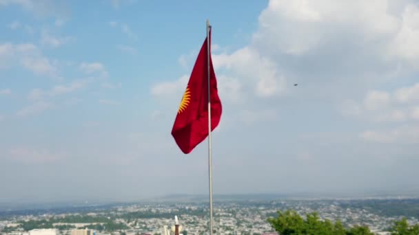 吉尔吉斯斯坦的国旗在风中飘扬 伴随着一些云彩和蓝天 在背景中可以看到奥什市 — 图库视频影像