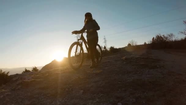 女の子は日没時に山の頂上で自転車を押している 背景に美しい渓谷の湖 — ストック動画