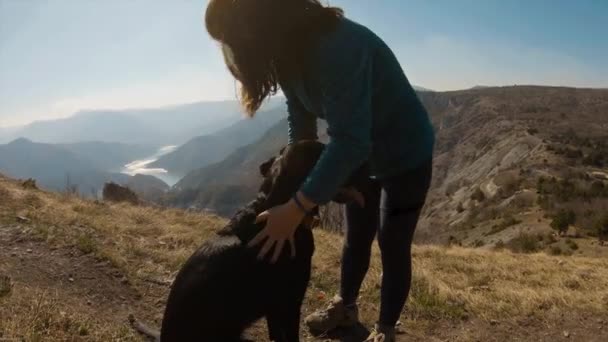 背景に美しい湖の渓谷と山の上に黒いラブラドール犬と抱きつく女の子 — ストック動画