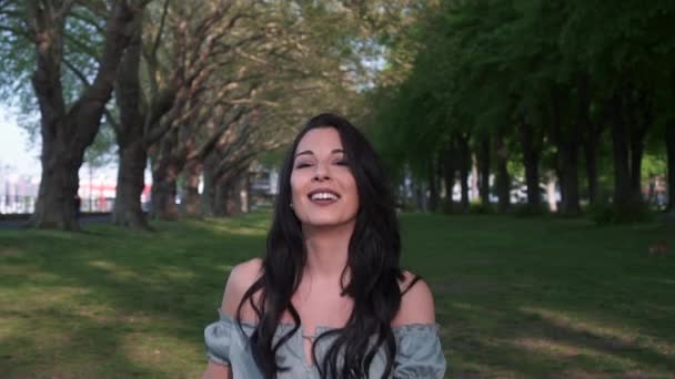 ロンドンの公園の木々の下を歩く黒い波状の髪をした魅力的で遊び心のあるラティーナの女性 カメラを見て 美しい笑顔で幸せに回転 — ストック動画
