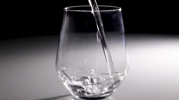缓慢运动的水被倒入带有深色背景的透明玻璃杯中 — 图库视频影像