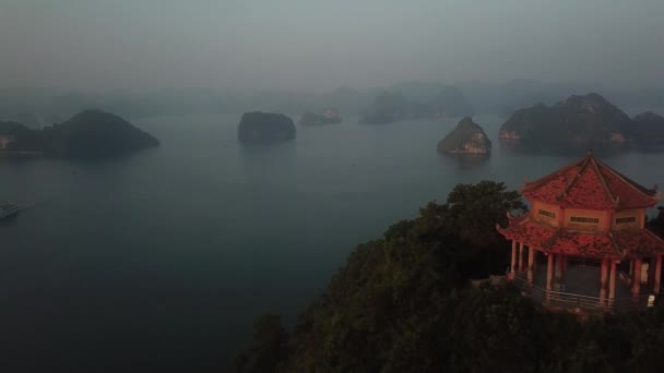 在夕阳西下的黄昏 空中的镜头缓缓掠过悬崖顶上的红色庙宇 露出下龙湾 — 图库视频影像