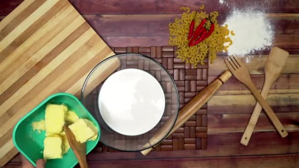 牛乳ボウルにバターを追加する上のビュー ボウルにマリネマカロニ 生のマカロニ 木製のスプーン 木製のへら 小麦粉 テーブルの上に圧延ピンとチリ — ストック動画