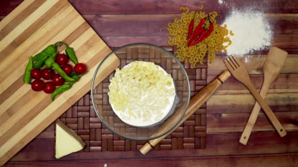 マカロニ 生のマカロニ 木のスプーン 木のへら 小麦粉 圧延ピン 冷凍チーズピースとテーブルの上に唐辛子を追加する上のビュー — ストック動画