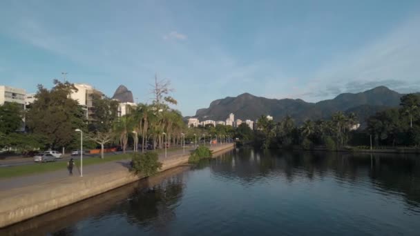 朝の運動をしたり自転車に乗ったりする人たちと一緒に リオデジャネイロ市内の湖沿いの空中後方のパンニング — ストック動画