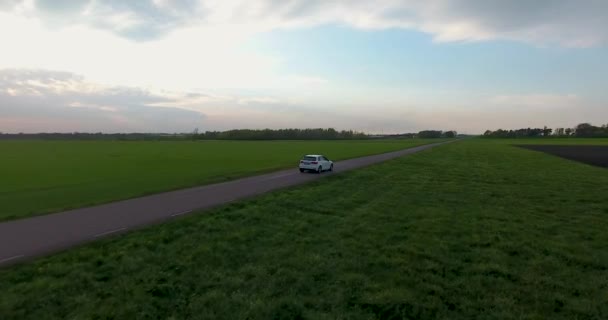 南スウェーデンの夕方の狭い田舎道で運転する白い車の空中ドローンショット Skne — ストック動画