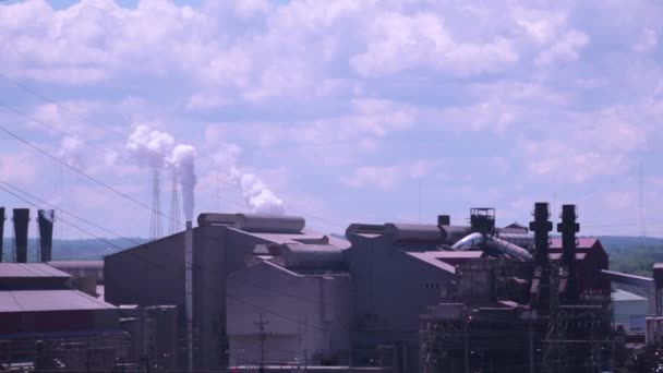 青空が広がる晴れた日に大気中の汚染を生み出す工場 白い煙と蒸気で雲が通り過ぎるサイロと金属製の機械が衝突して原料を生産します — ストック動画