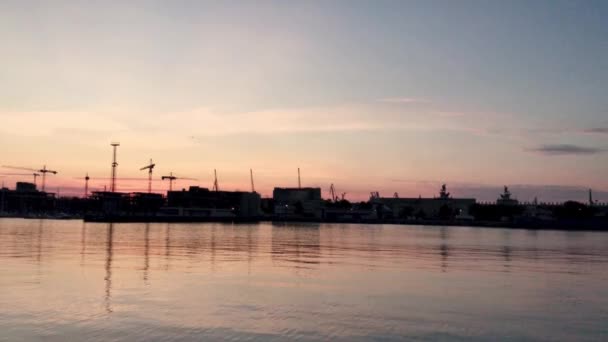 日落在港口的海岸上 鸟瞰着橙色的天空 背景高高的起重机在海滨的建筑工地上建造了新的建筑 海上的低猎鹰 Gdynia Pomorskie — 图库视频影像