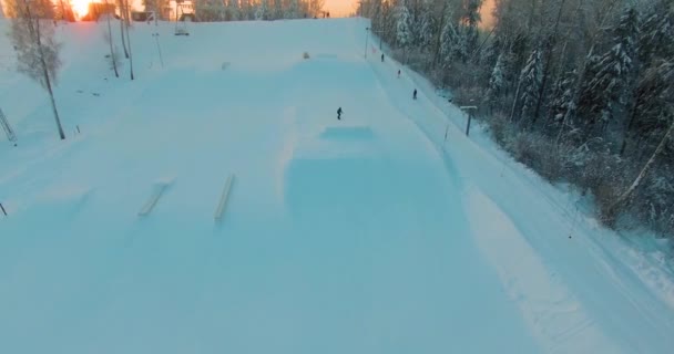 Främre Flygbild Snowboardåkare Som Hoppar Från Sluttning Terrängpark Vid Solnedgången — Stockvideo