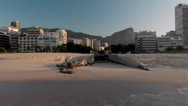 都市の湖とレブロンのビーチと海を結ぶ運河からの空中バックアップ日の出を背景にリオデジャネイロのCorcovado山に入ってくる波を明らかにする — ストック動画
