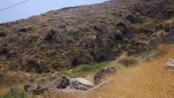 サントリーニ島のレッドビーチ近くの山の丘によっていくつかの暗い神秘的な洞窟の広いショットを開催ギリシャ — ストック動画