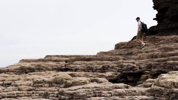Ein Junger Mann Geht Einem Strand Über Große Felsen — Stockvideo