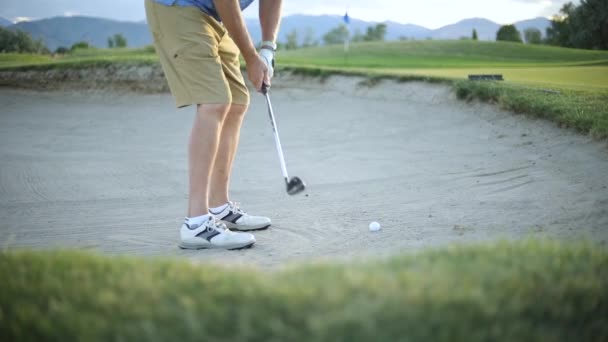 ゴルフボールを打つゴルファーの後ろにスローモーションショット砂トラップから入れ緑に ゴルファーは素敵なリゾートゴルフコースで遊んでいます — ストック動画