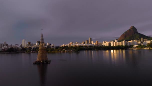 2018年世界で最も高い空中アプローチ都市湖の上からリオデジャネイロのより広い都市の中で背景に2人の兄弟の山と日の出に浮かぶクリスマスツリー — ストック動画