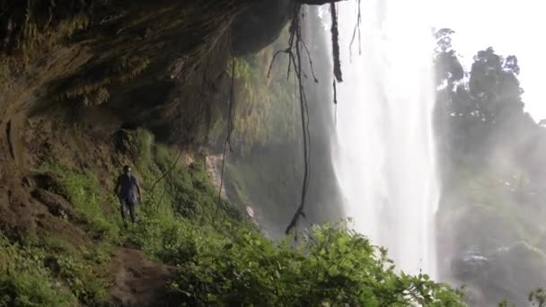 在热带瀑布后的洞穴中行走的非洲人 — 图库视频影像