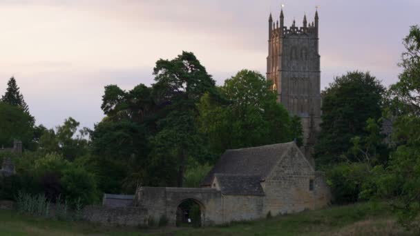 コッツウォルズの典型的なイギリスの田園風景で 古い石造りの建物とゴシック様式の教会の塔が見えます イギリス — ストック動画