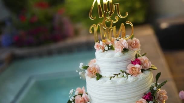 夏の結婚式のレセプション中にプールのすぐ隣の台座に座って美しく装飾された花のウェディングケーキのショット — ストック動画