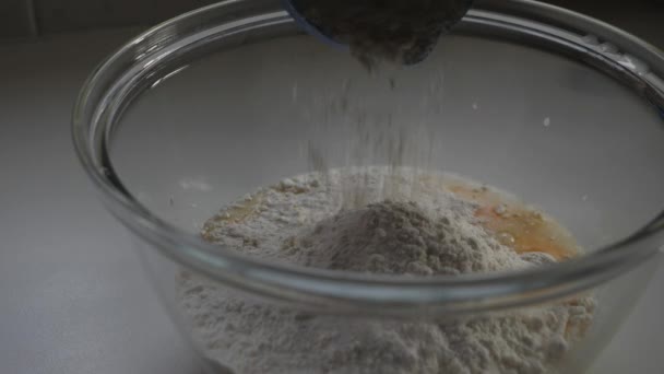 人们把面粉从蓝色的量杯撒入玻璃碗中烘烤鸡蛋的混合物中 慢动作宏观 — 图库视频影像
