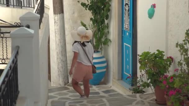 穿着夏天健行服装的女孩 带着蓝色的门和植物走过典型的希腊狭窄小巷 — 图库视频影像