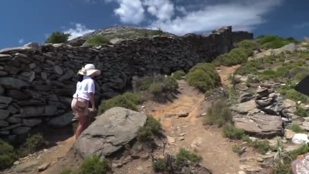 身着夏日登山服头戴帽子的女孩走在山墙旁边的小径上 相机右盘指向标志 — 图库视频影像