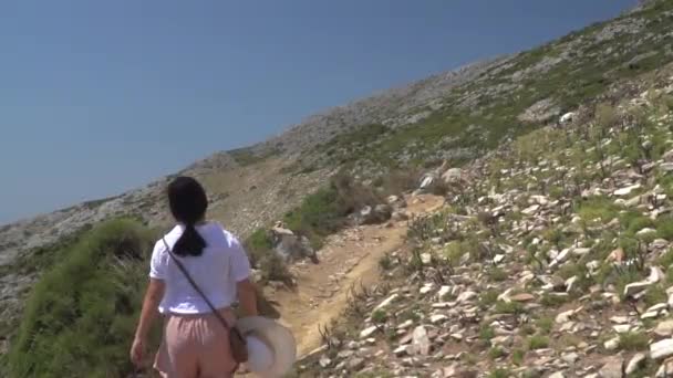 接着是穿着夏天登山服的女孩在荒山野岭中走在路上的镜头 — 图库视频影像