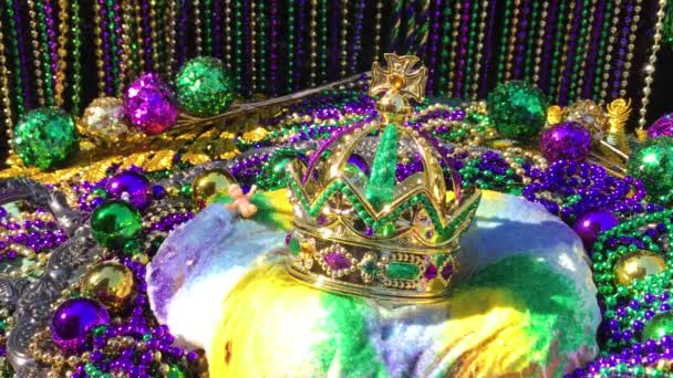 Mardi Gras王ケーキの上に影を動かす王冠とカラフルなビーズに囲まれた小さな赤ちゃん — ストック動画