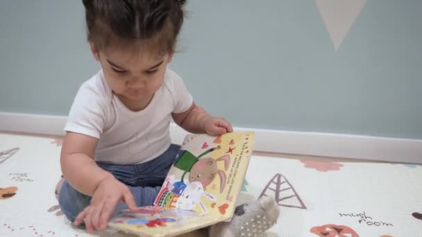 床に座っている幼児は 図された子供向けの本を読み ページをめくります 快適ゾーン 家庭での教育 — ストック動画