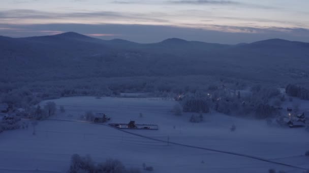 遠くに山と木製のキャビンと雪の牧草地の上にドローンのパンニング — ストック動画