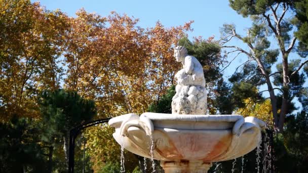 在马德里 西班牙 的雷蒂罗公园拍摄了一个喷泉剖面 水滴到侧面 在最上面 一个神话般的男人坐在那里 冬日阳光灿烂 在有些树叶呈橙色的树后面 可以看到树木 — 图库视频影像