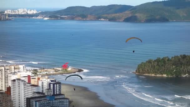 サントス ブラジルビーチ ウォーターフロントの建物の上を飛ぶパラシュート付きパラグライダー — ストック動画