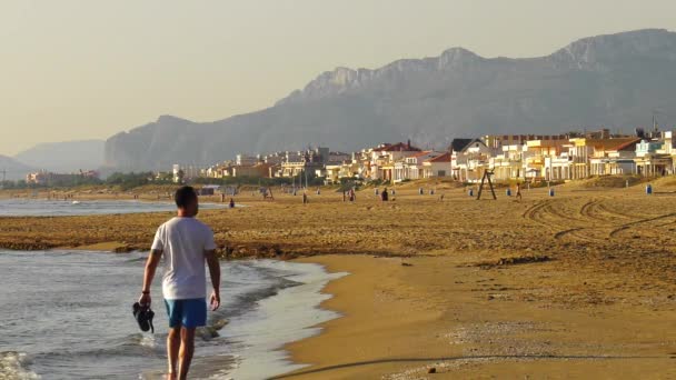 スペイン 沿岸の町 砂浜の海岸線を裸足で歩く若い男 — ストック動画