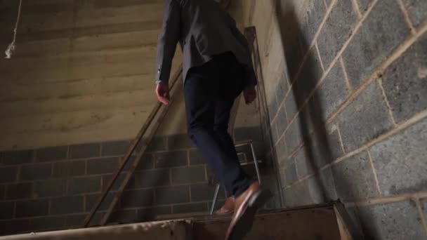 頂上に何があるかを発見するために建物の塔の上に階段のセットを歩くスーツの男 — ストック動画