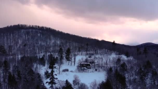 カラフルな夕日の間にバーモント州の雪の山に囲まれた納屋付きキャビン — ストック動画