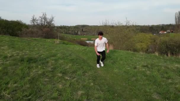 青年男子翻筋斗 在绿色室外场地跑步 慢动作鼓声射击的空中场景 — 图库视频影像