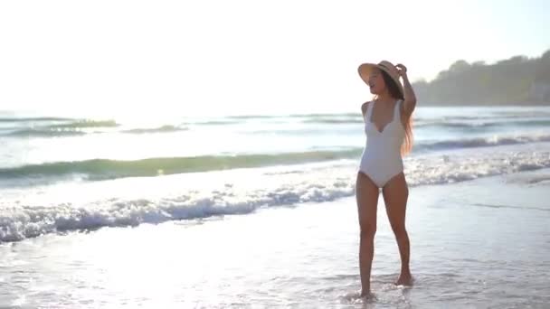 白い水着と夏の帽子でセクシーな女性熱帯の海の波によってサンディビーチを歩く スローモーション — ストック動画