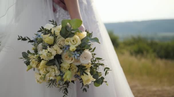 花嫁立っている彼女の結婚式の花束花で草原の外で儀式の後に白いドレスアップジンバルショットで夏の曇りの日 — ストック動画